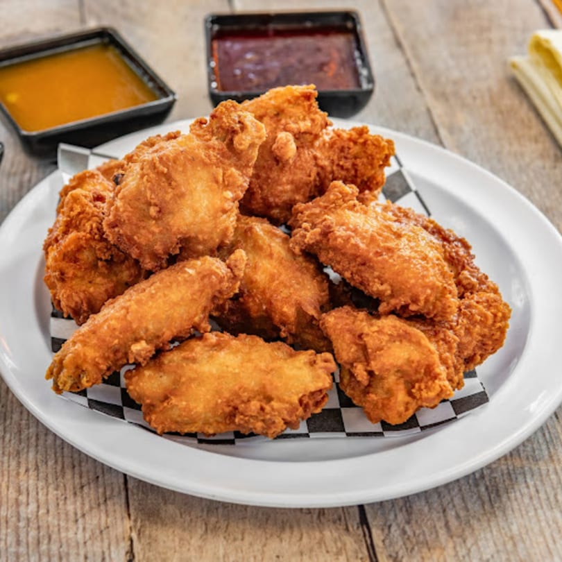 Crispy fried chicken wings on a white plate with checkered paper, with two dipping sauces in the background.