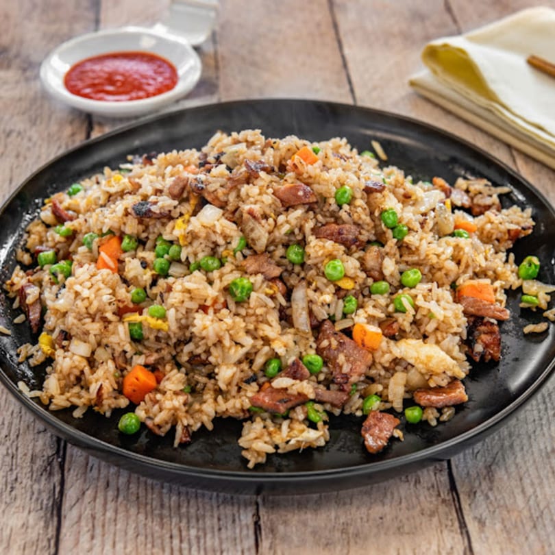 Happy Pho Teriyaki's fried rice with peas, carrots, and meat, served with a side of chili sauce.