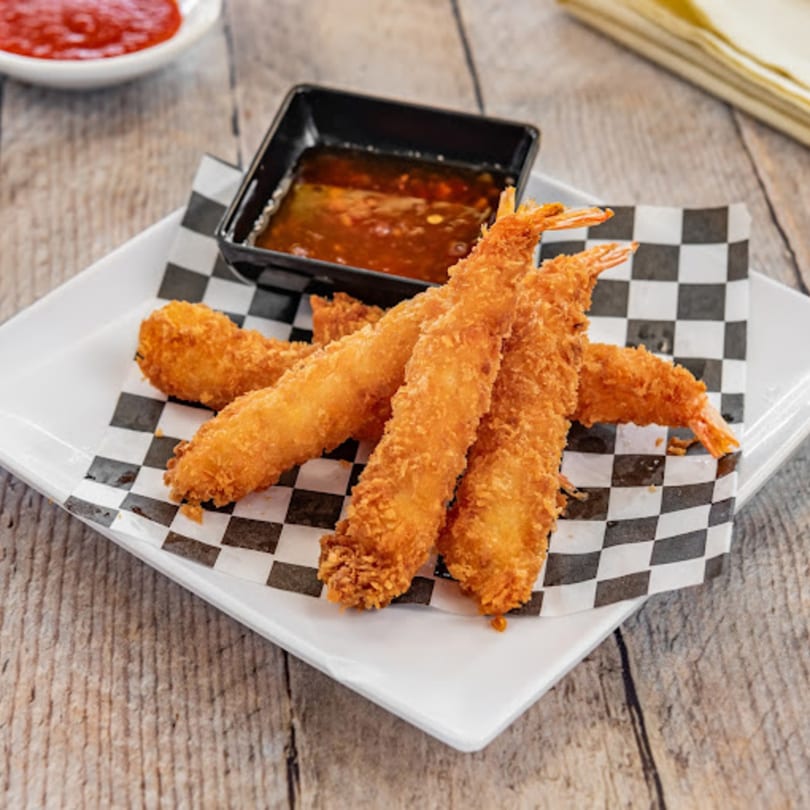 Crispy fried shrimp with a side of sweet chili dipping sauce on a white plate with checkered paper.
