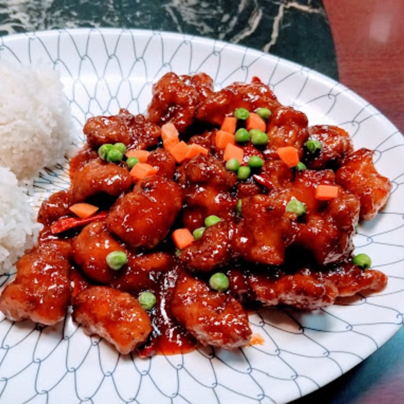 Sweet and sour chicken with peas, carrots, and white rice on a patterned plate.