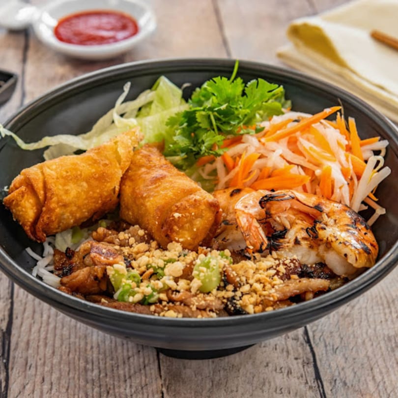 A Vietnamese vermicelli bowl with grilled shrimp, egg rolls, pork, and vegetables.