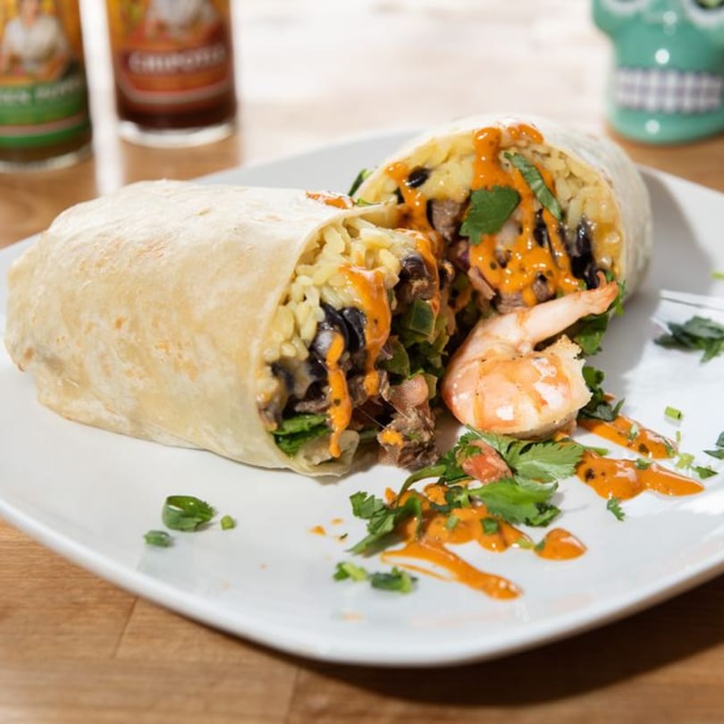 A large burrito, cut in half, revealing rice, beans, and meat, with shrimp and sauce.